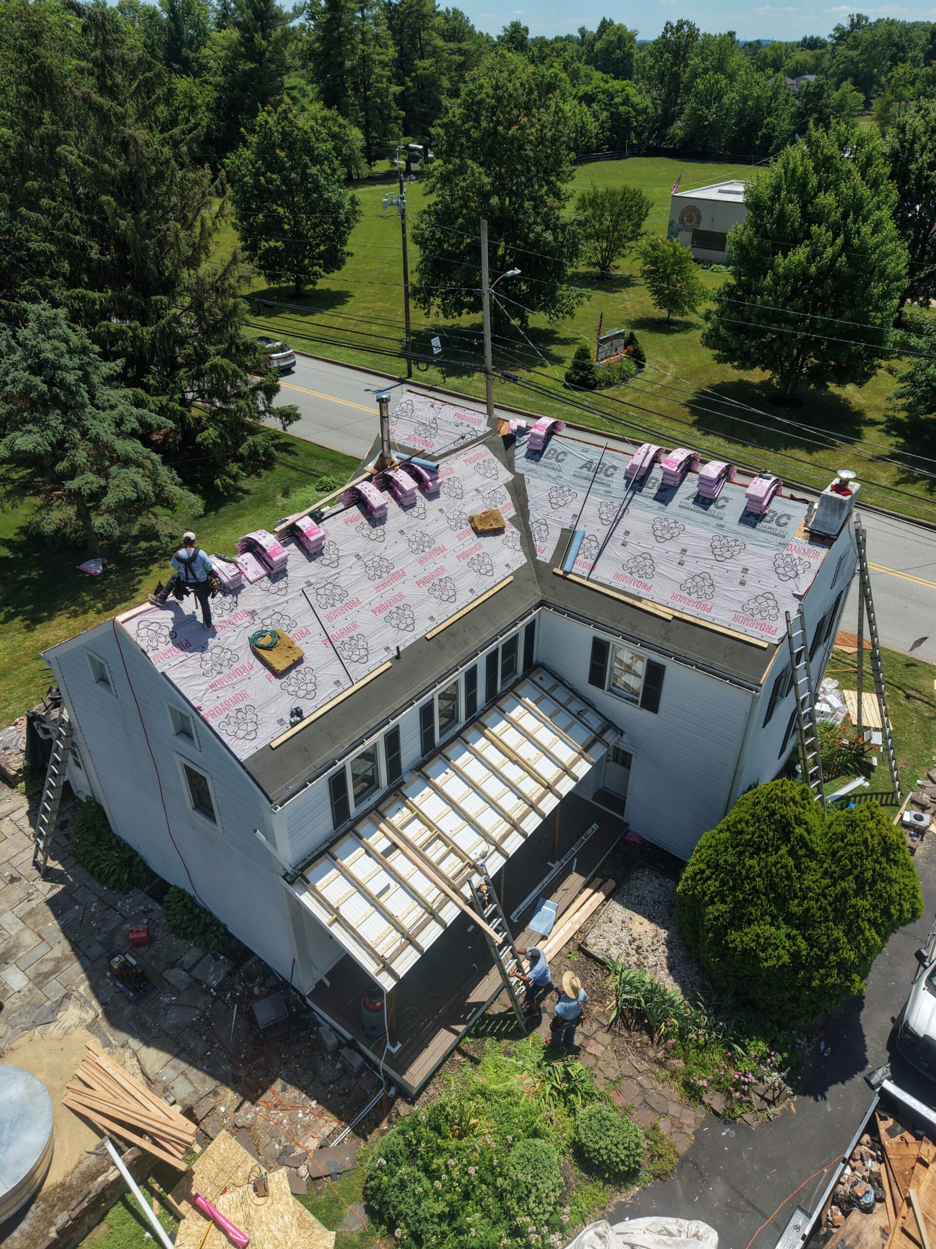 default Workers replacing roof on a white house with pink underlayment, surrounded by trees and a road in Harleysville, PA.